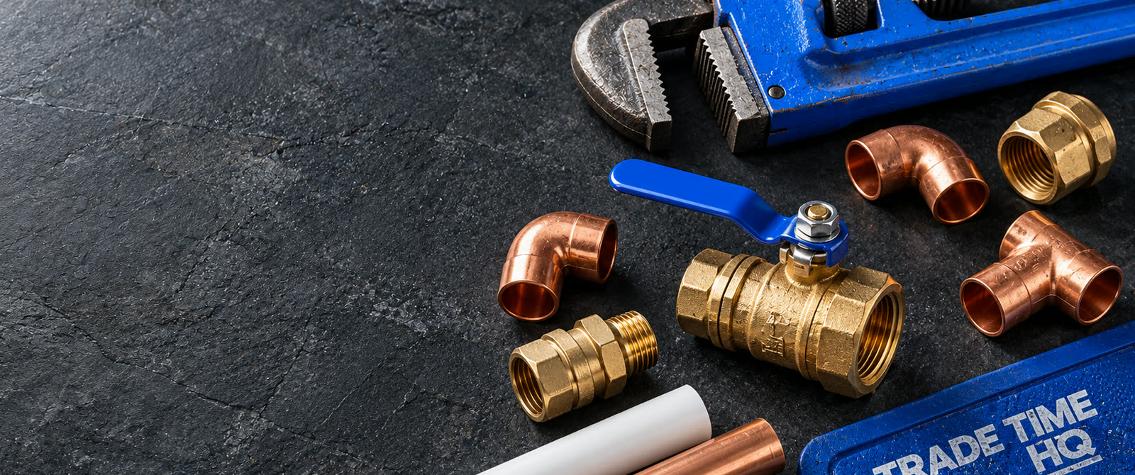 Illustration: a blue pipe wrench, a brass ball valve, copper fittings and PEX on a slate workbench